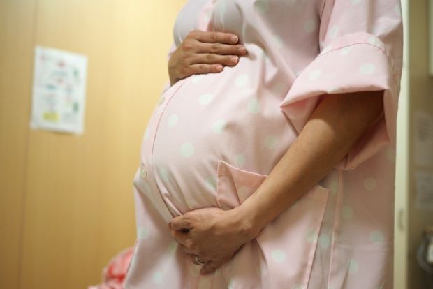 お腹に手を当てたピンクの病衣を着た妊婦の写真